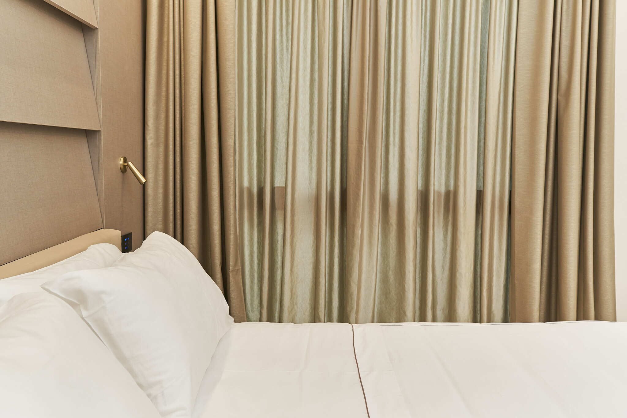 A hotel room with a bed, curtains, and a control panel on the wall.