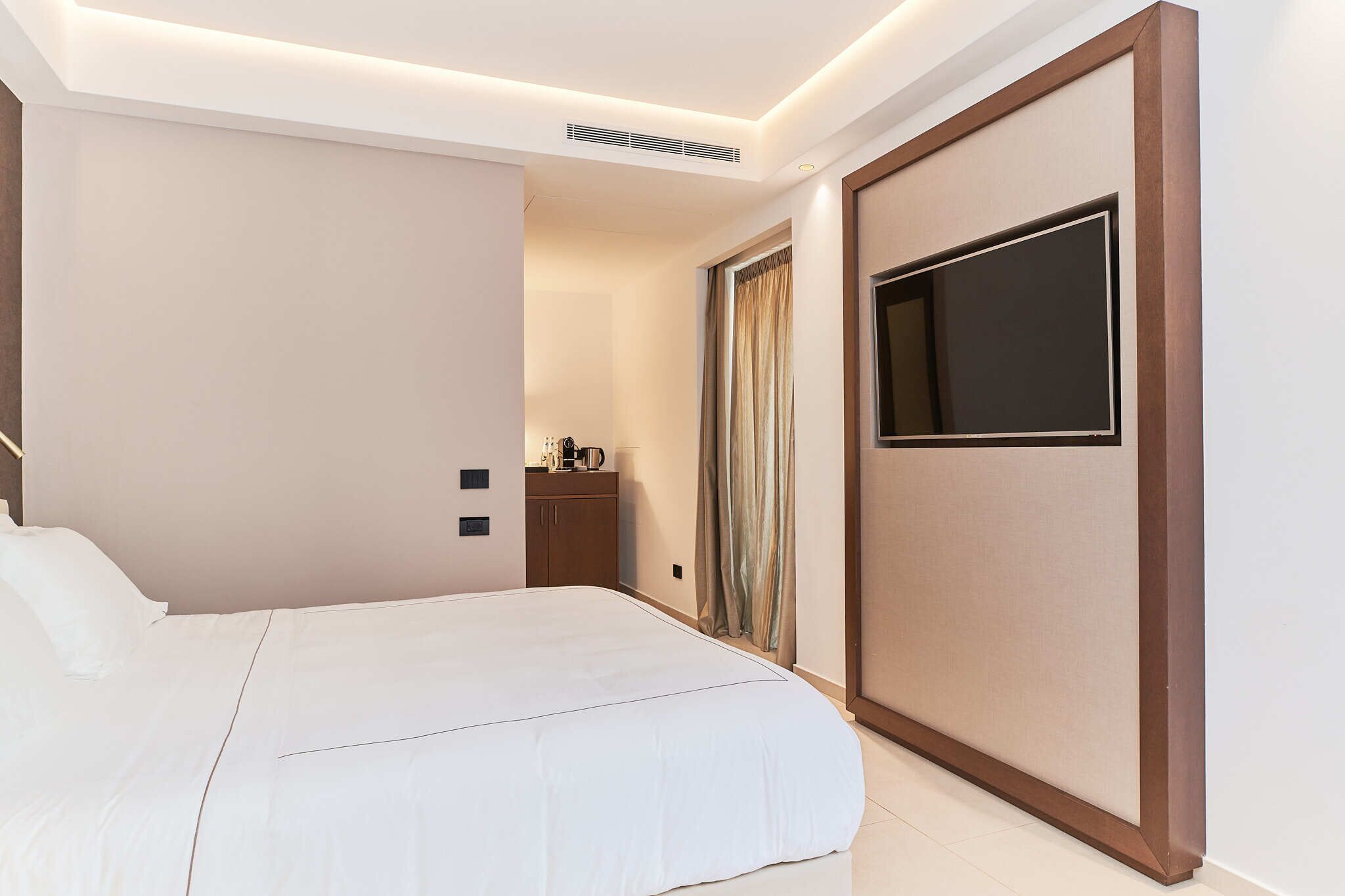Een hotelkamer met een groot bed, een aan de muur bevestigde televisie, een garderobe en een klein tafeltje met een waterkoker.