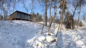 Moderni mökki, jossa on puinen terassi ja näkymä puilla ympäröidylle järvelle.