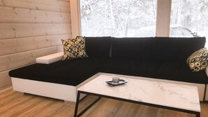 Moderni olohuone, jossa on musta kulmasohva, valkoinen sohvapöytä ja kuviollisia koristetyynyjä.