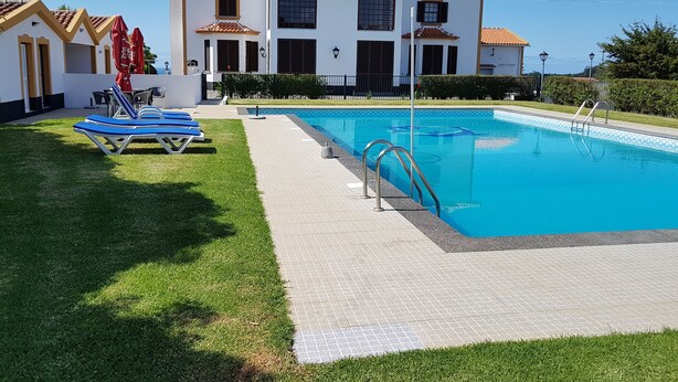 A pool area with a clear blue pool, a lounge area with blue chairs, and a large building with a tiled roof. - Casa Marques (Angra do Heroismo)