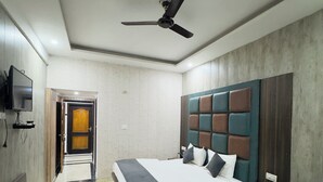 A modern hotel room with a large bed, a desk, a chair, a TV, and a ceiling fan. - Hotel Jagdish Residency (Reasi)