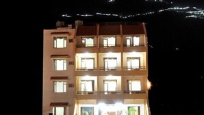 A multi-story hotel with a central entrance, multiple balconies, and a parking area with several cars. - Hotel Jagdish Residency (Reasi)