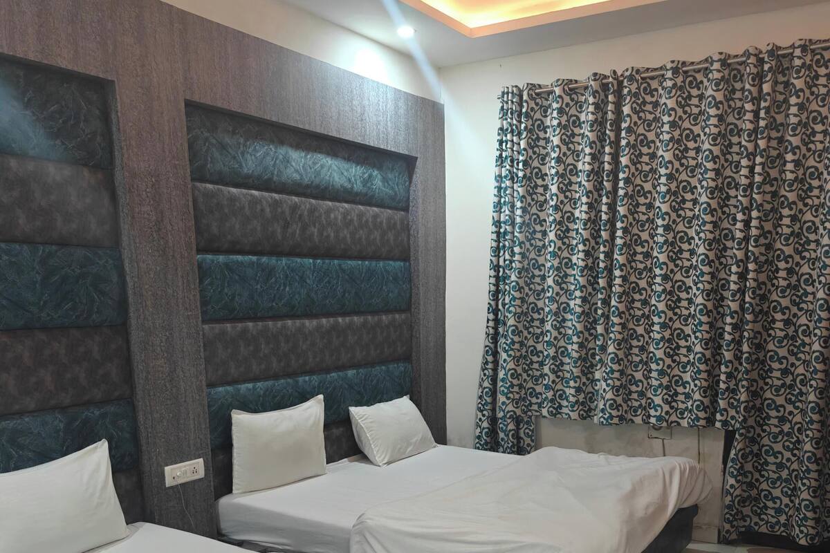 Habitación de hotel con dos camas individuales, cabecera con diseño texturizado, cortina estampada y suelo de baldosas.