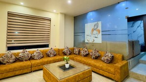 A modern living room with a sectional sofa, a glass coffee table, and a large abstract painting on the wall. - Hotel Jagdish Residency (Reasi)