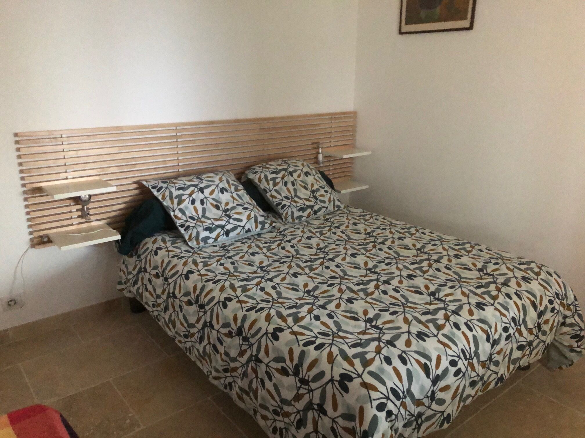 A bed with a leaf-patterned bedspread, a wooden headboard, and a bedside table with a lamp.