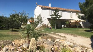 Une maison blanche avec un toit en tuiles, une terrasse avec des meubles d’extérieur et un jardin agrémenté de cactus et de rochers.