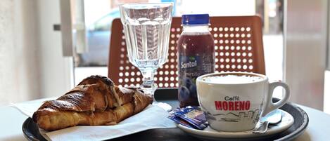 A tray with a croissant, a glass of water, a bottle of Santal, and a cup of coffee labeled "Caffè MORENO".