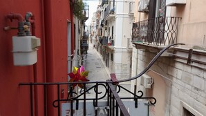 A narrow urban street with buildings on both sides, a metal gate, and a red wall with pipes. - Il Cavalliere Bed & breakfast (Barletta)