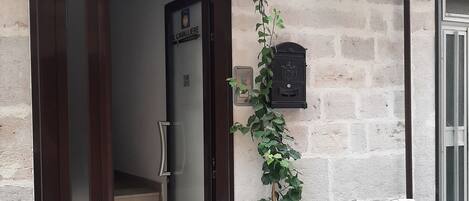 Entrada de un edificio con puerta de cristal, una escalera que conduce al interior, un buzón rojo y una bicicleta estacionada afuera.