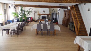 Un comedor con una mesa larga dispuesta para seis personas, rodeada de sillas. Hay una chimenea con repisa, y una escalera visible a la derecha.