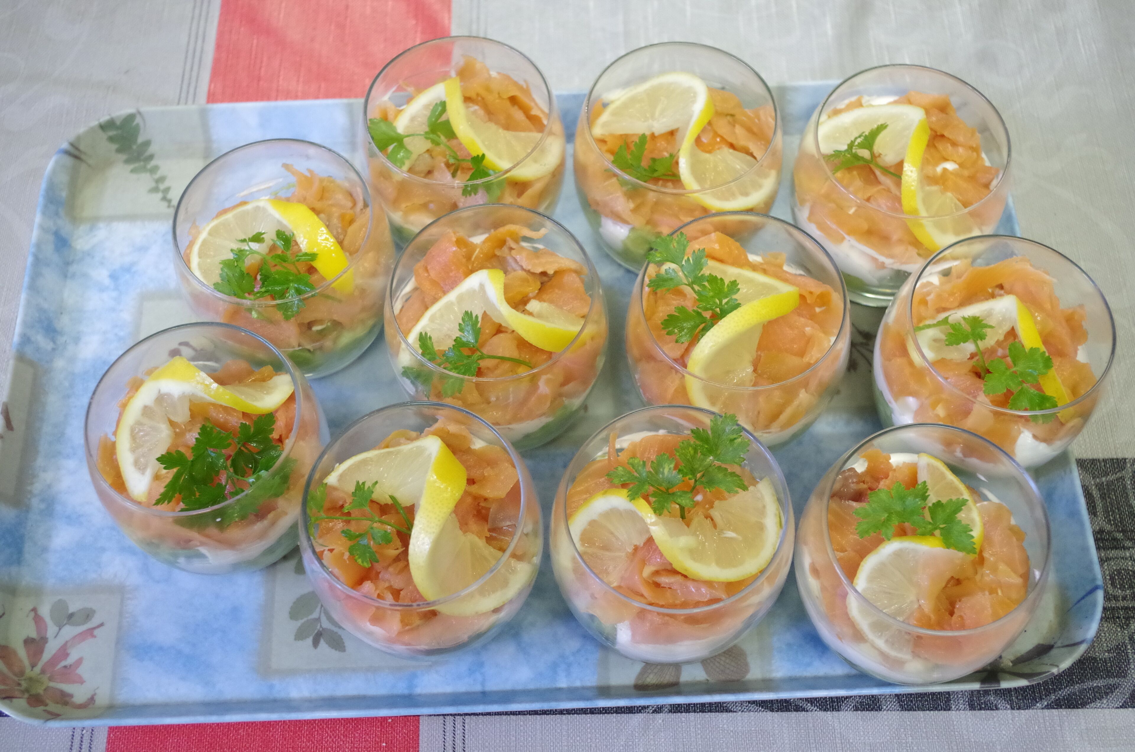 A tray with multiple glasses containing a salmon dish garnished with lemon and parsley.