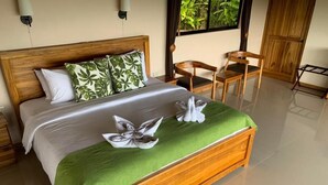 A neatly made bed with a green bedspread and two towels, wooden headboard, and a wooden chair in a well-lit room with a large window. - Drake Bay Greenleaf (Drake Bay)