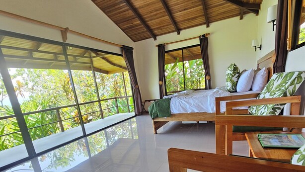 A spacious room with a large bed, a smaller bed, and a seating area with wooden chairs and green cushions. - Drake Bay Greenleaf (Drake Bay)