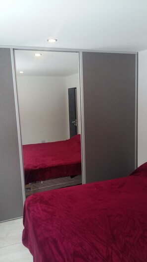 A bedroom with a red bedspread, a sliding door closet, and a ceiling light.