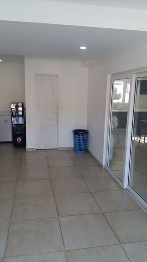 A spacious room with a tiled floor, a white door, a blue laundry basket, and a small appliance unit.