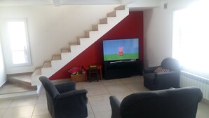 A living room with a TV, two armchairs, a small table, and a staircase with a red accent wall.