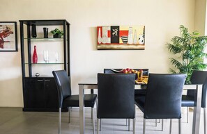 Un coin repas comprenant une table à manger noire, quatre chaises noires, un meuble vitré contenant des objets décoratifs, un tableau accroché au mur et une plante en pot.