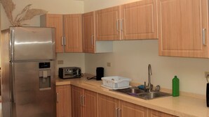 A compact kitchen with wooden cabinets, a stainless steel refrigerator, a toaster, and a sink. - Crown Point Condo (Crown Point)