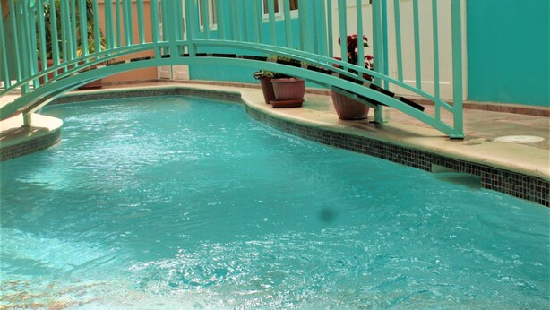 A turquoise pool with a metal bridge, surrounded by a building with white-framed windows and a tiled floor. - Crown Point Condo (Crown Point)