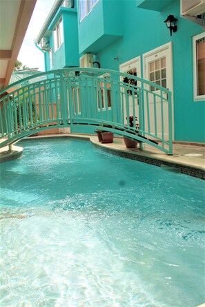 A turquoise pool with a metal bridge, surrounded by a building with white-framed windows and a tiled floor.