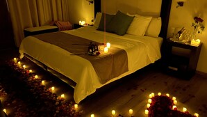 A dimly lit bedroom with a bed, bedside tables, and a nightstand. - Hotel Villa Murano (San Cristóbal de las Casas)