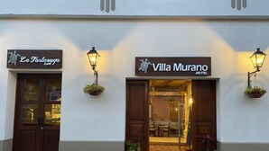 A building with two entrances, one labeled "La Farturga Cafe" and the other "Villa Murano Hotel". Both entrances have wooden doors and are flanked by wall-mounted lanterns. - Hotel Villa Murano (San Cristóbal de las Casas)