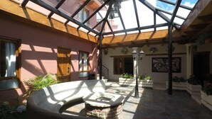 A sunlit courtyard with a stone fire pit, a wooden bench, and potted plants. - Hotel Villa Murano (San Cristóbal de las Casas)