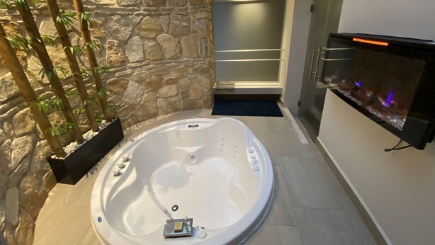 A modern bathroom with a stone wall, a hot tub, and a built-in fireplace. - Hotel Villa Murano (San Cristóbal de las Casas)