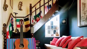 Een woonkamer met een houten trap, een gitaar en een bank met rode kussens. Vlaggen hangen aan de trapleuning.