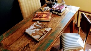Een houten eettafel met een lamp, boeken en een telefoon. Een stoel staat ernaast.