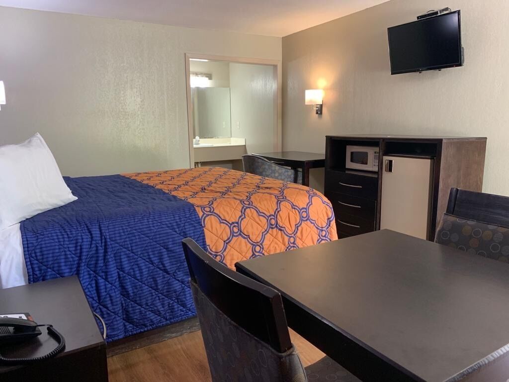 A hotel room with a bed, a desk, a chair, a microwave, a television, and a mirror.
