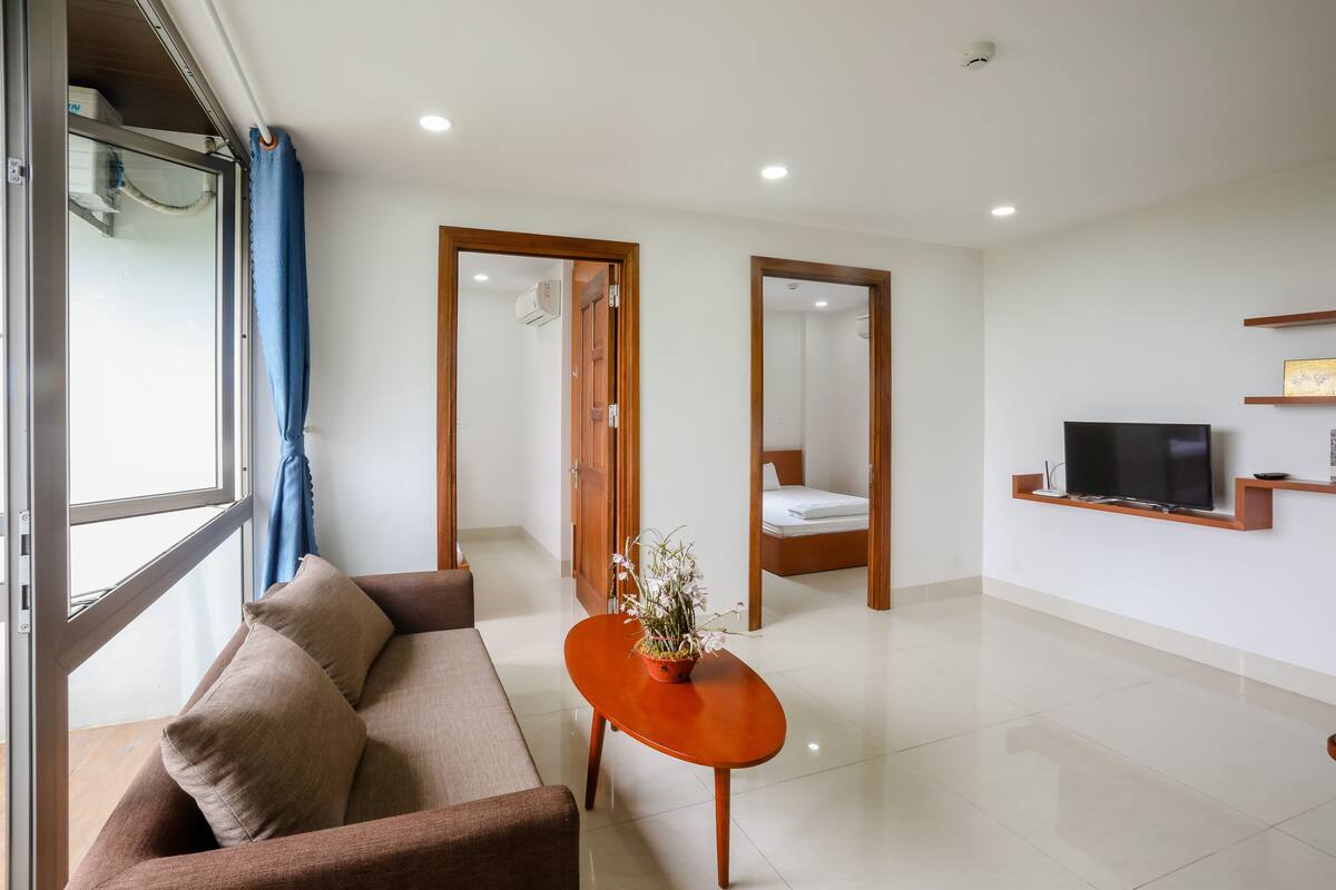 Una habitación de hotel moderna con un sofá, una pequeña mesa con una planta, un televisor en un estante y una cama.