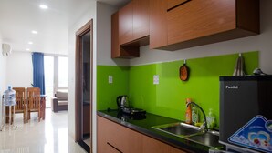 Una cocina moderna con armarios de madera, salpicadero verde y encimera negra. Se observa un fregadero, un hervidor y un refrigerador.