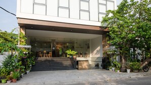 Un edificio moderno con entrada de cristal, mesas al aire libre y diversas plantas en macetas.