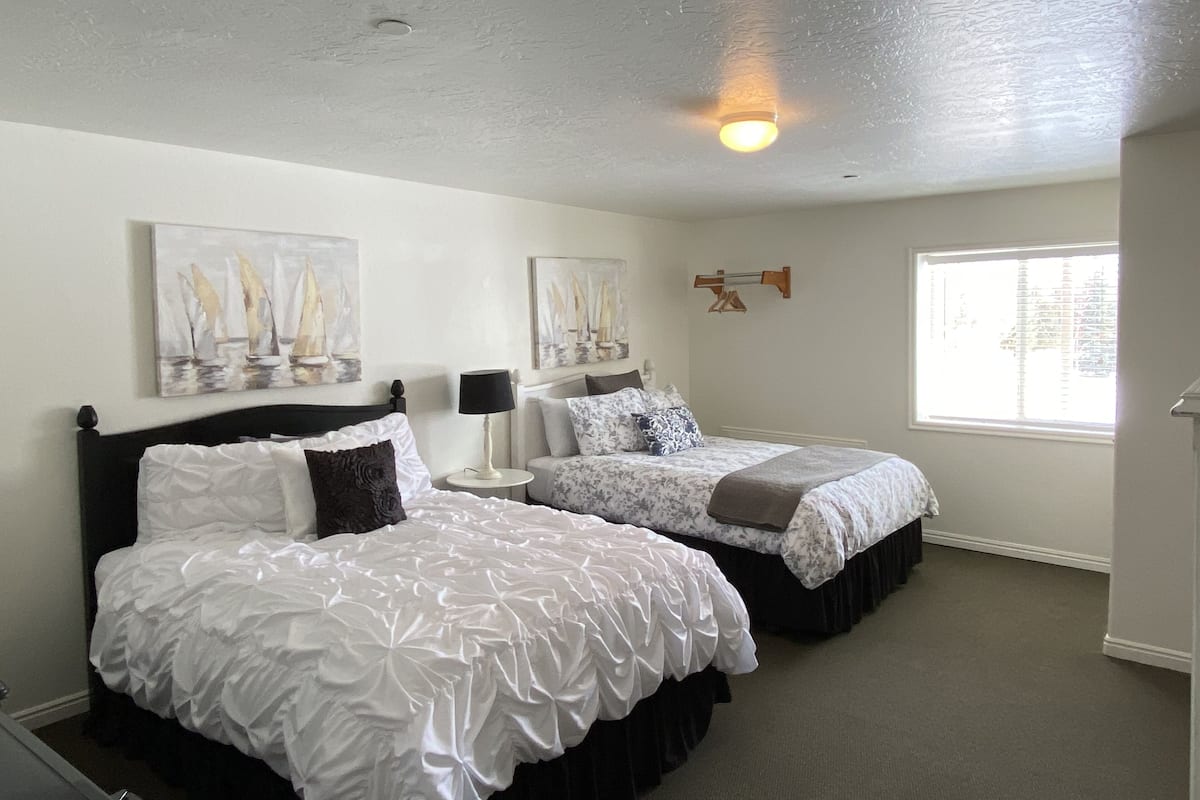 A bedroom with two beds, a window, and artwork on the walls.