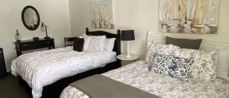 A bedroom with two beds, a dresser, a mirror, and artwork on the walls.