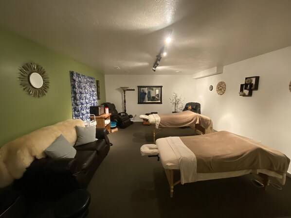 A room with two massage tables, a sofa, a lamp, and a mirror on the wall.