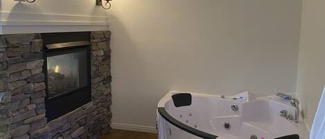 A modern bathroom with a stone fireplace, a freestanding bathtub, and wall-mounted lighting.
