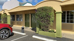 A building with a green door, a parking space with a red car, and a small window. - Holiday Motel (Morgan Hill)