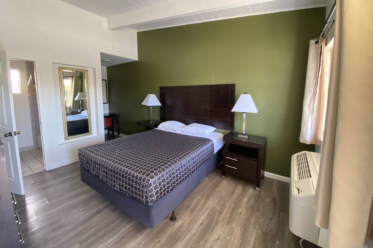 A hotel room with a large bed, two bedside tables with lamps, a wooden floor, and green walls.