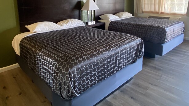 A room with two beds, a nightstand, a lamp, and a window with curtains. - Holiday Motel (Morgan Hill)