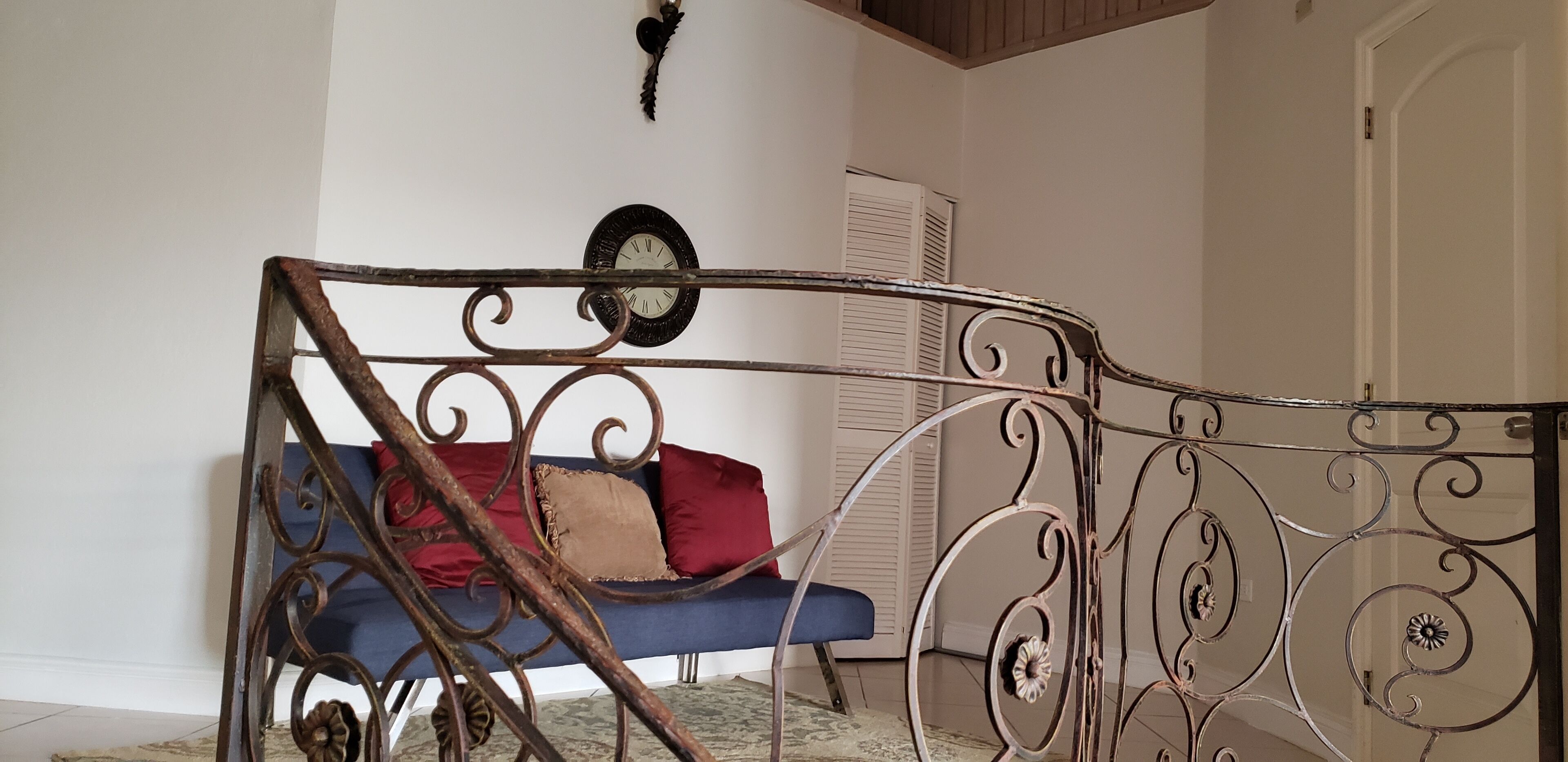 A room with a blue sofa, a decorative metal railing, a wall clock, and a white door.