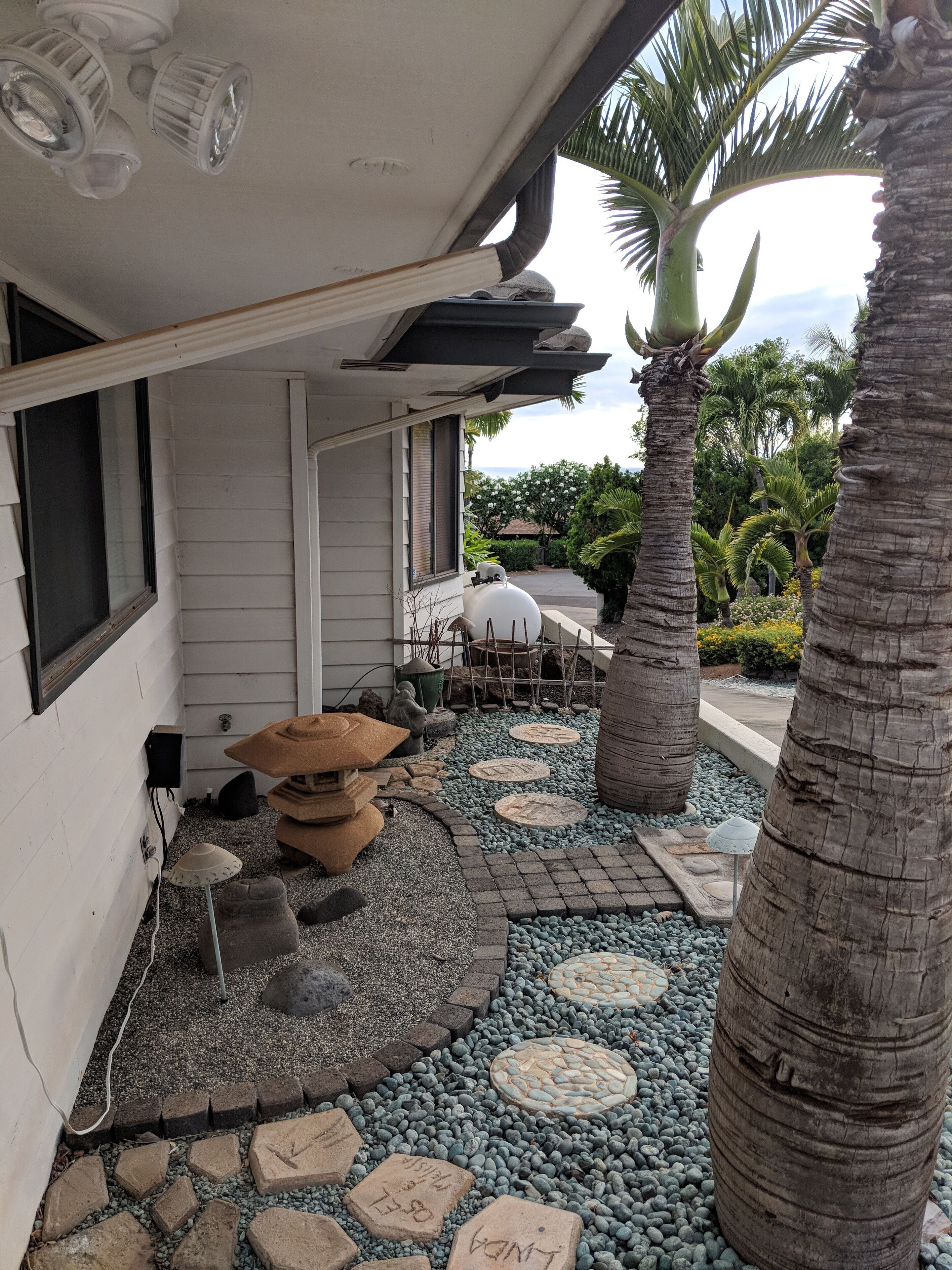 A covered outdoor area with a stone pathway, palm trees, and a small seating area.