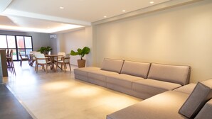 Una sala de estar moderna con un sofá color crema, una mesa de comedor con sillas y una planta en maceta.
