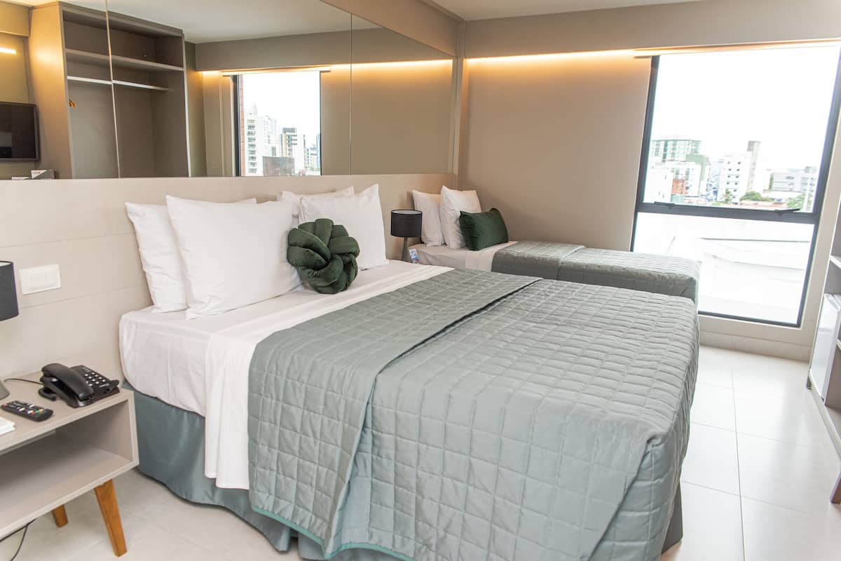 A hotel room with two beds, a desk with a phone, and a large window with a city view.