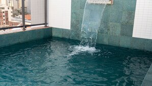 Una piscina con una cascada, rodeada de paredes con azulejos y vistas a la ciudad.