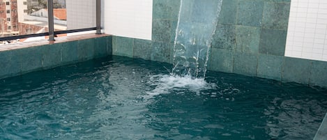 Une piscine agrémentée d’une cascade, entourée de murs recouverts de carreaux et offrant une vue sur la ville.