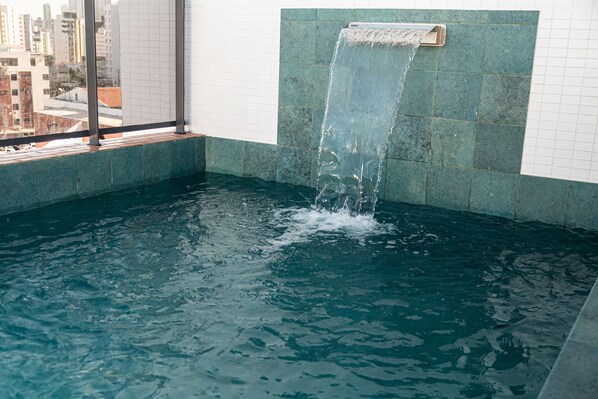 Una piscina con una cascada, rodeada de paredes con azulejos y vistas a la ciudad.