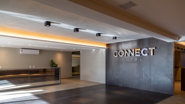 Una moderna zona de recepción de hotel con un mostrador grande, una unidad de aire acondicionado en la pared y un letrero que dice "CONNECT HOTEL".